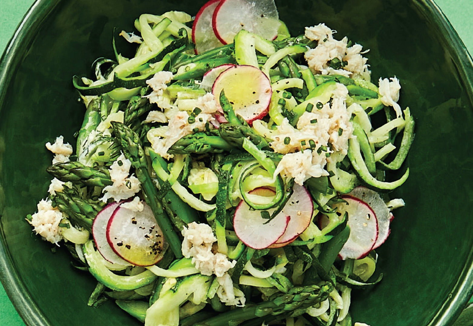 A bowl of zucchini noodles dressed with blue swimmer crab meat and thinly sliced radishes