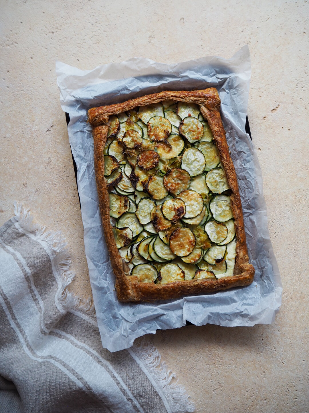 Cooked zucchini and ricotta tart on baking paper, lying on top of a tea towel located in the bottom left corner.