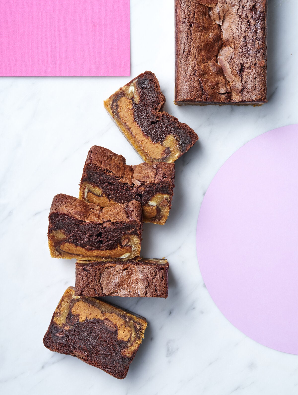 5 pieces of the biscoff cookie brownie laid out in a trail in the centre of the page with the remaining loaf in the top right corner.
