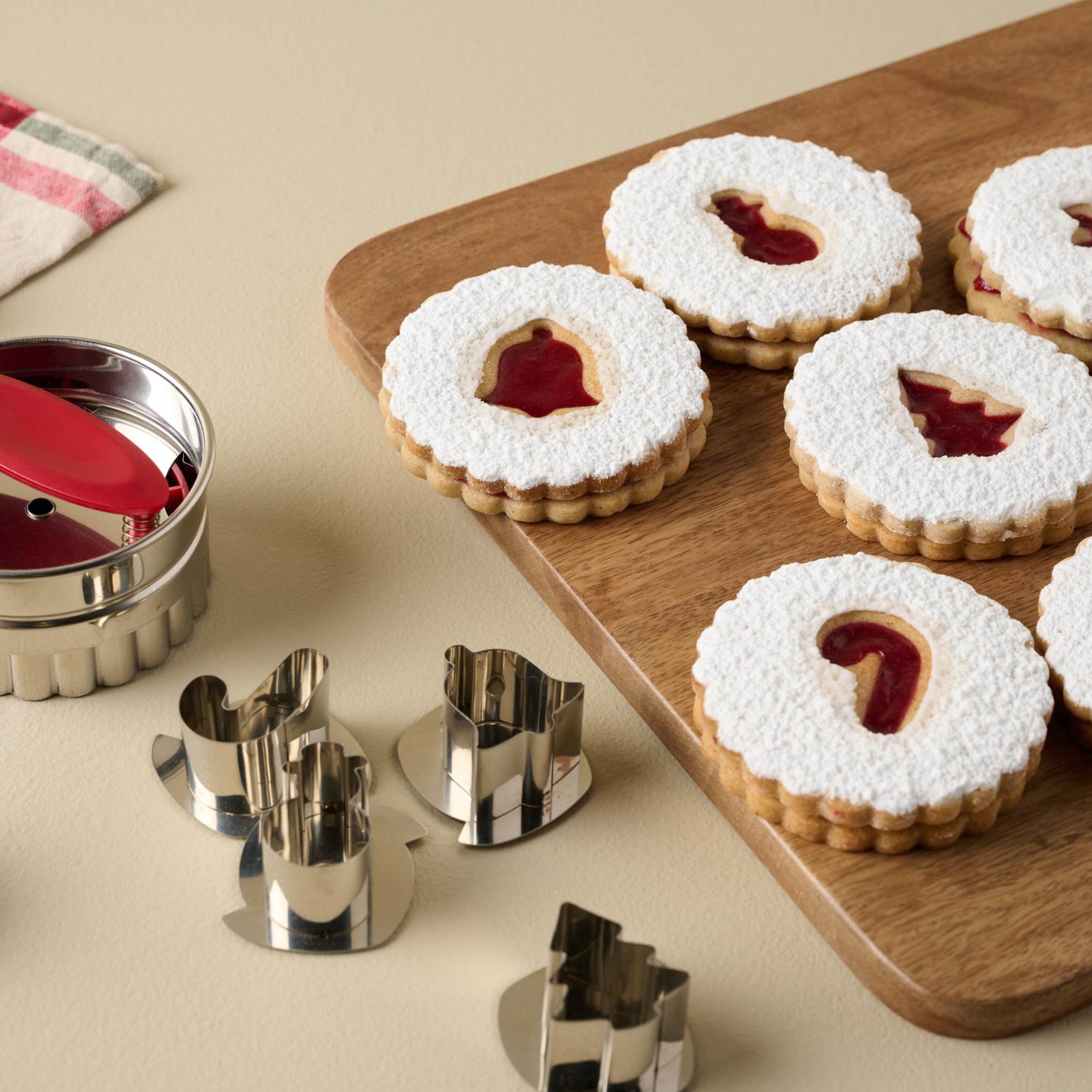 Linzer cookies on a wooden board next to a cookie cutter set.