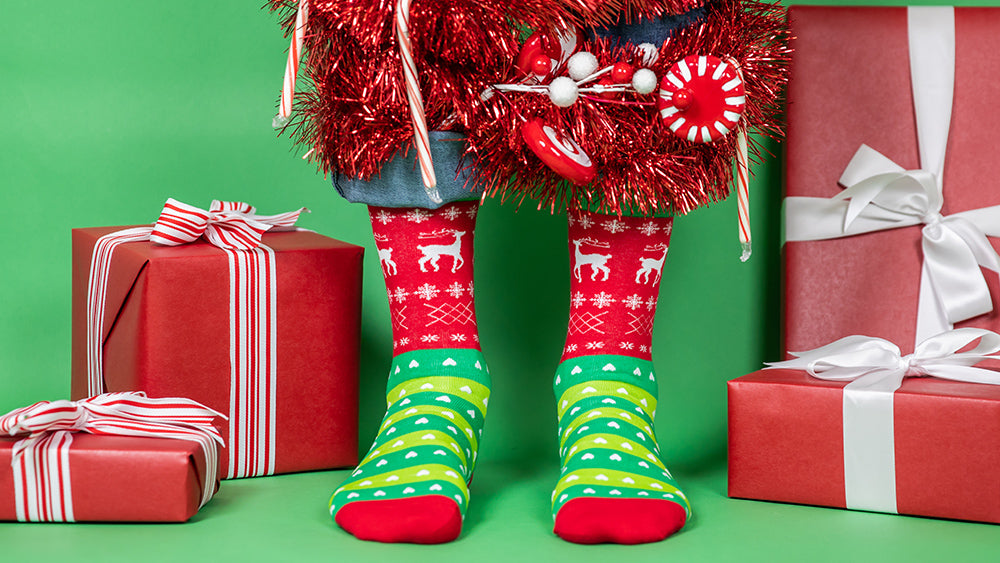 Model wearing Tacky Christmas Sweater socks and standing in front of presents