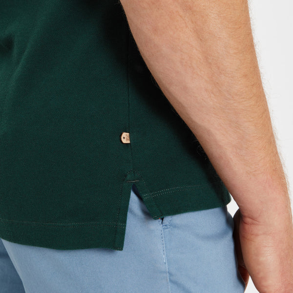 man wearing forest green pique polo shirt and navy trousers showcasing casual menswear style