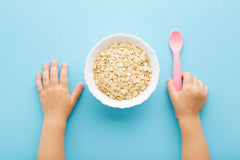 Baby's Hands Beside Bowl of Oats on Blue Table