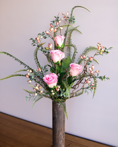 An arrangement with pink roses and fern leaves