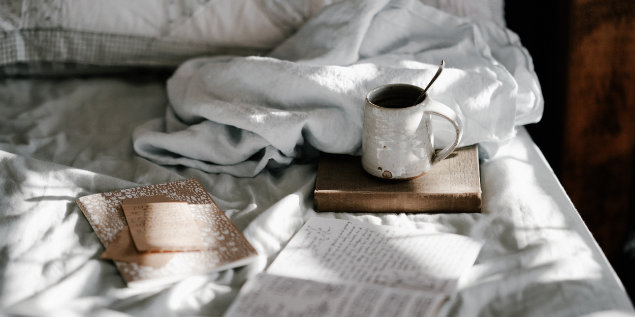 coffee-cup-and-diary-resting-on-bed-sheets