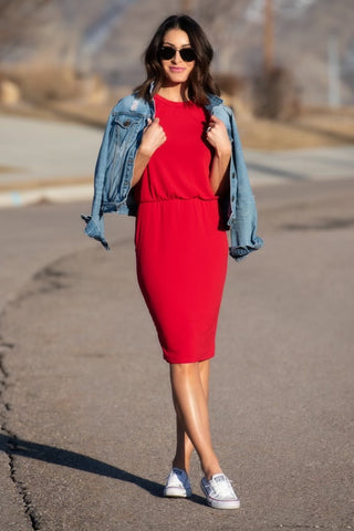 Female standing outside in a road. She's wearing a red dress with a jean jacket draped over her shoulders.