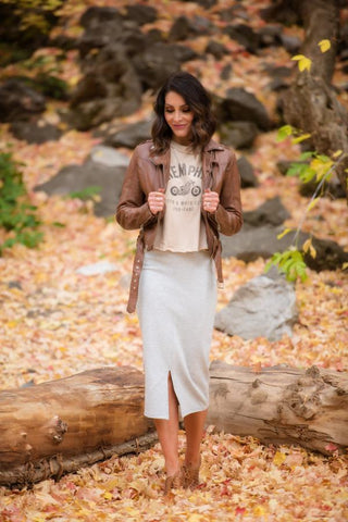 Woman standing in leaves wearing leather jacket with graphic tee and skirt