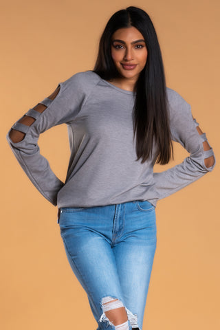 Brunette girl wearing a long sleeved shirt with slits in the arm and light distressed jeans.