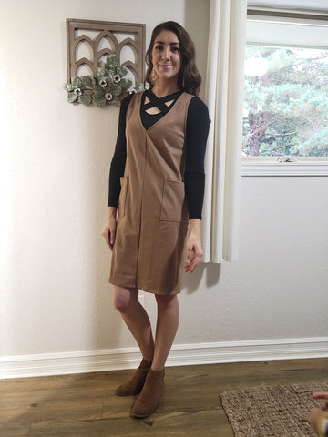 Woman posing for a photo in camel overall dress with long sleeve black shirt