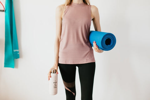 Crop sportswoman carrying sport mat and bottle of water before exercising