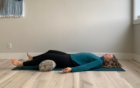 Supported Savasana with a yoga bolster to reduce back pain
