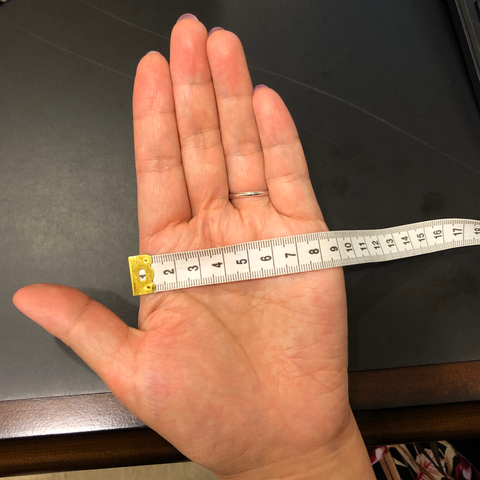Place a ruler/ tape measure on your open palm from you index knuckle to the right most knuckle.