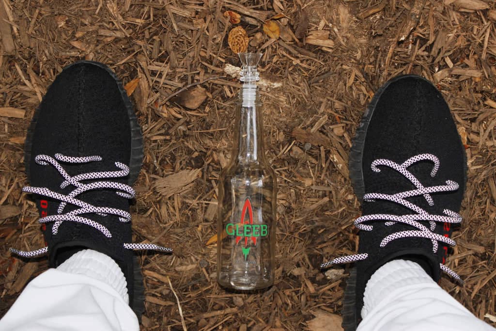 Feet standing on wood chips next to a glass gravity bong