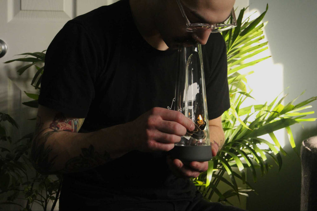 man holding glass bong and lighter