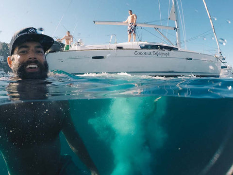 man with beard swimming by sailboat