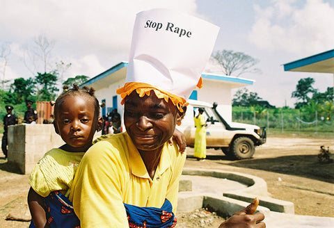 Zwei schwarze Menschen sind zu sehen, einer trägt einen Papierhut mit dem Aufdruck "Stop Rape" (Stoppt Vergewaltigung)