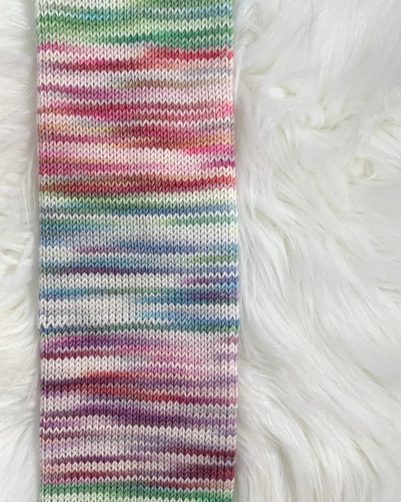 A little creative doodle. A knitted tube of yarn with four variegated white-and-colour sections. The top section is mostly green, the next is pink, then blue, then purple, then back to a bit of green at the bottom.