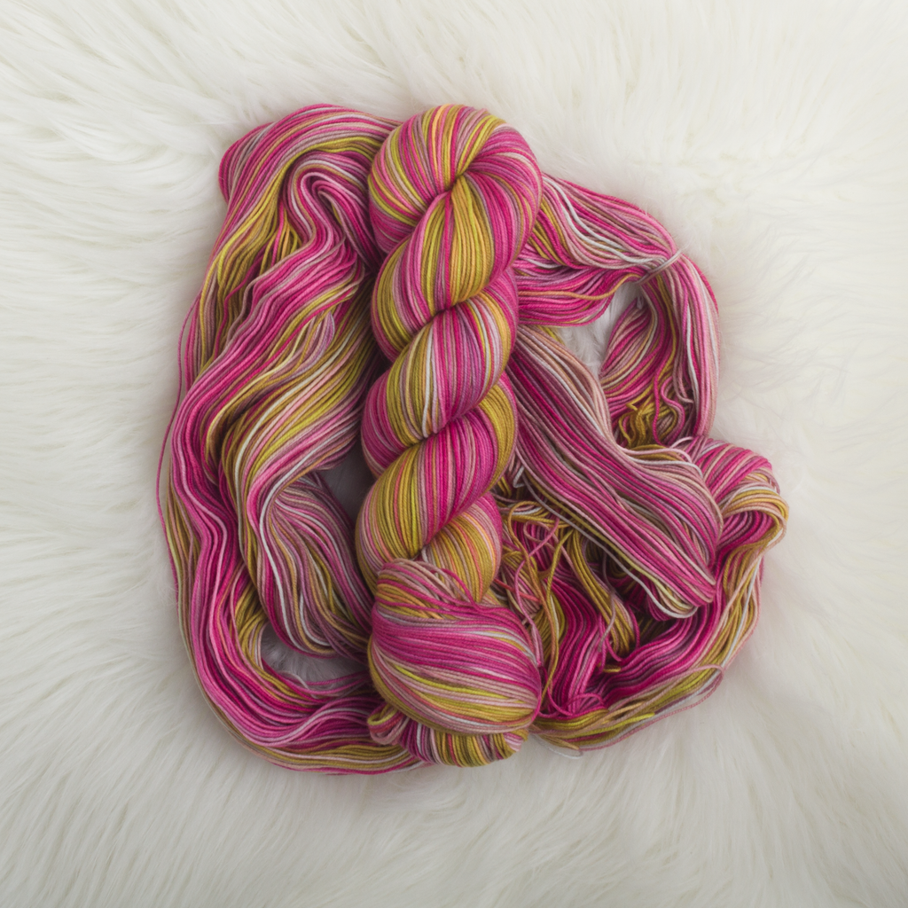 A twisted skein of yarn sitting on a loose pile of more of the same yarn. The colours are pink and yellow.