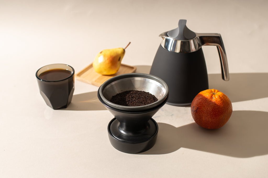 An Able Kone metal coffee filter in a Ratio ceramic dripper, next to a Ratio Thermal Carafe in matte black.