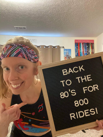 Woman holding sign "Back to the 80s for 800" and wearing a Ponya Bands Bamboo Terry Lined Sweatband