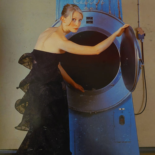 Blonde Swedish model in black lace evening gown with a volant back opening a blue vintage washing mashine