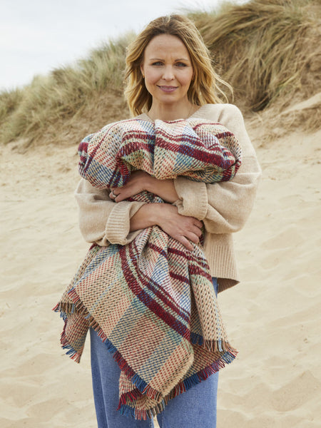 a women on a beach holds a cosy warm recycled blanket