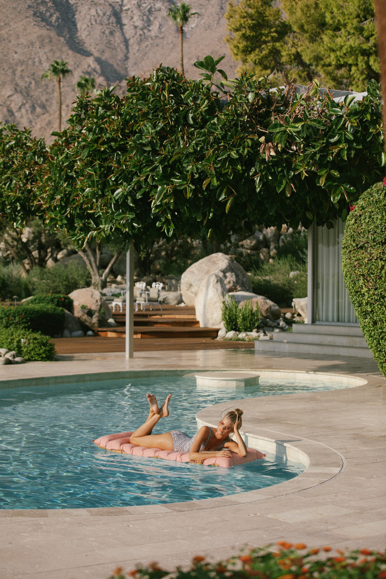 Spell Garden Party campaign model, Kim Riekenberg, posing on a lilo in a pool while wearing the navy ditsy floral Poppy One Piece with a low scooped back. 