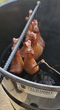 Chicken legs hanging over Pit Barrel Cooker rod while cooking