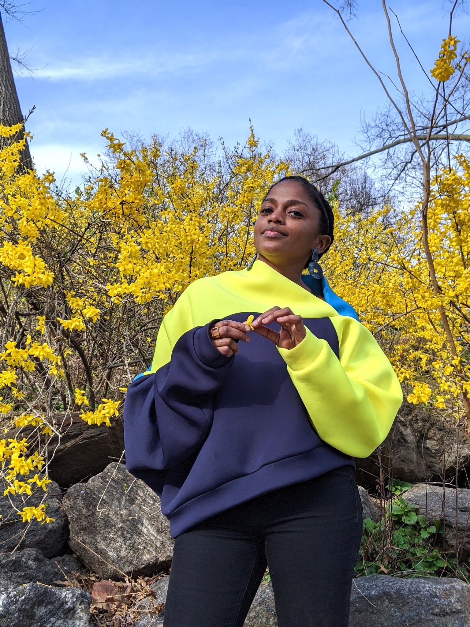 Outdoor portrait of Nathalie Jolivert in yellow and blue sweater with yellow flowers behind her