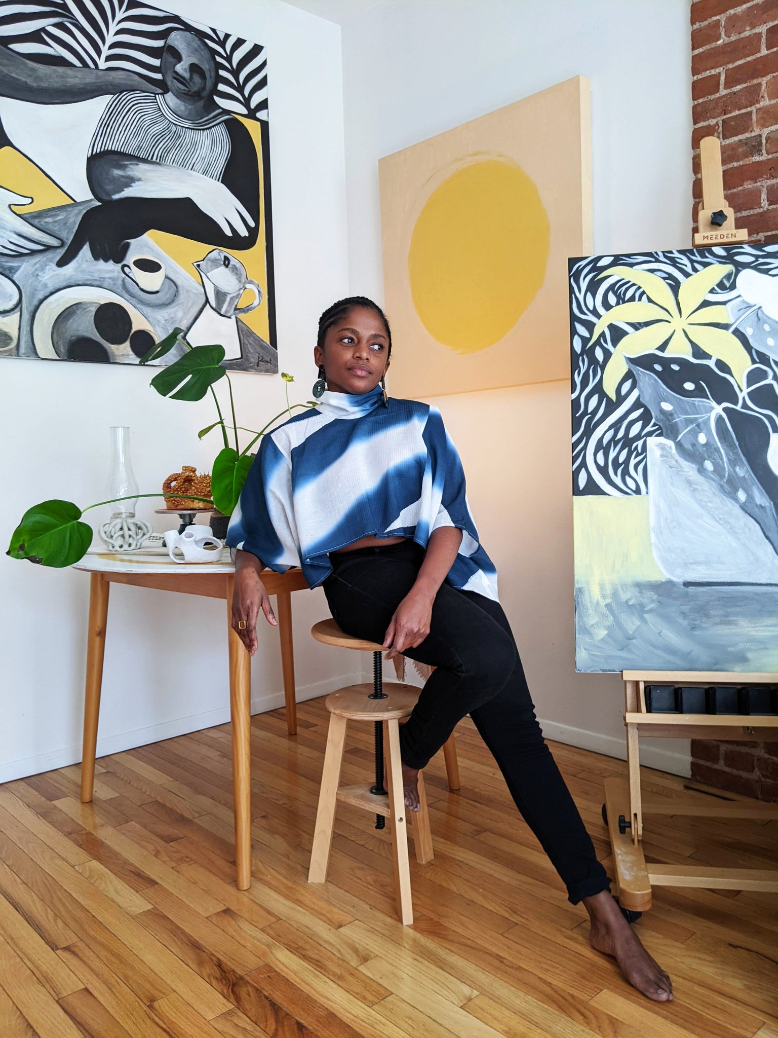 Portrait of Nathalie Jolivert sitting on stool in front of her paintings