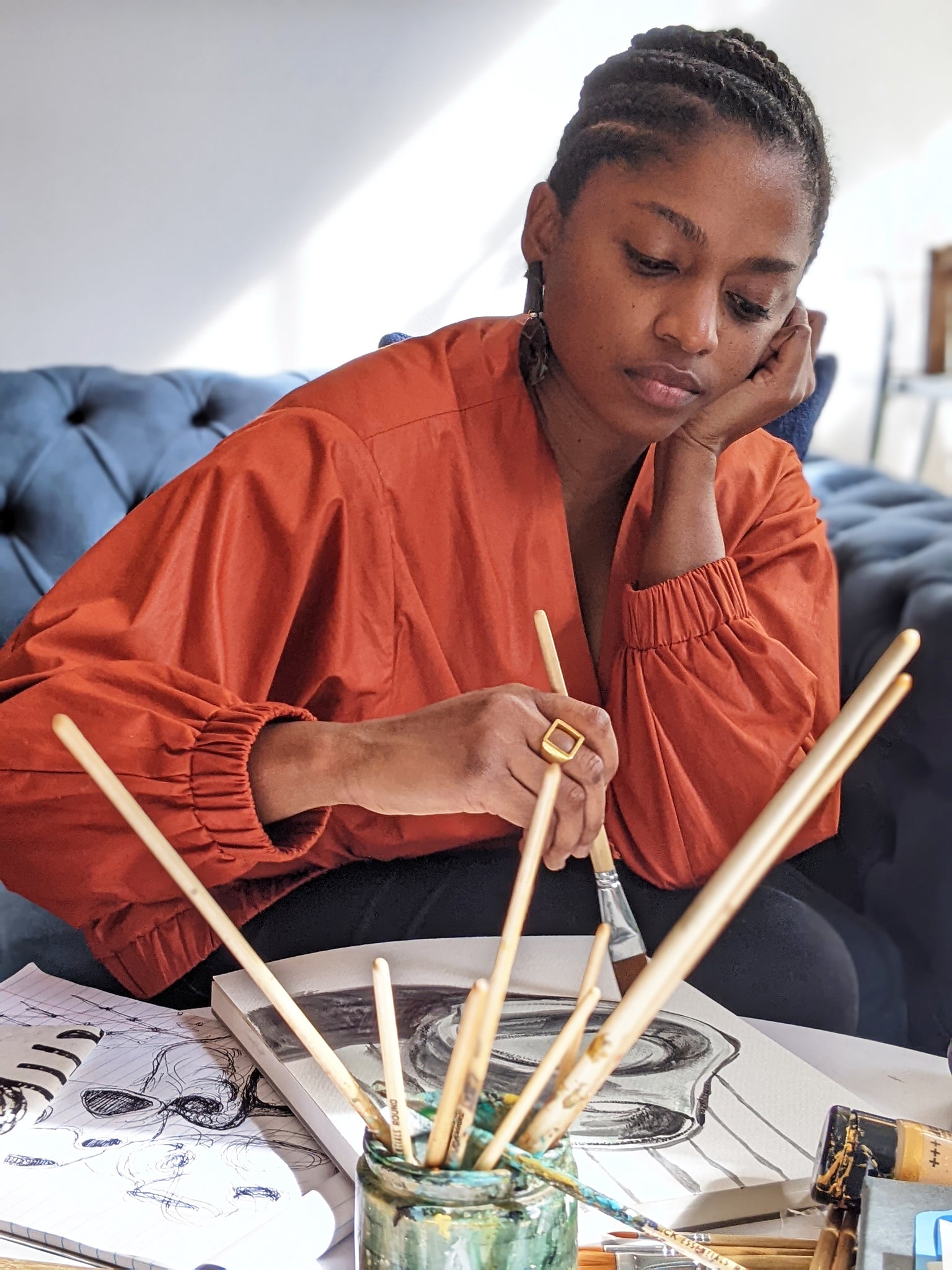 Portrait of Nathalie Jolivert in burnt orange jacket painting on sketchbooks