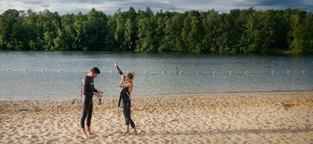 Two swimmers getting ready to go into the water by adjusting their wetsuits