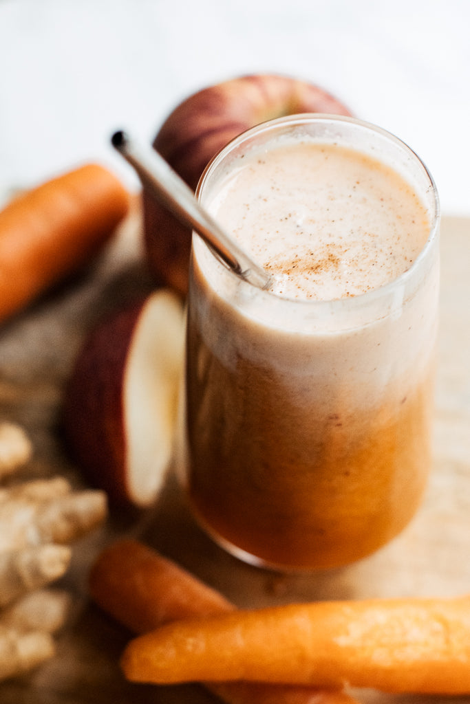 Warm orange Super Skin Smoothie topped with yoghurt in a glass with straw surrounded by Carrot, apple, ginger