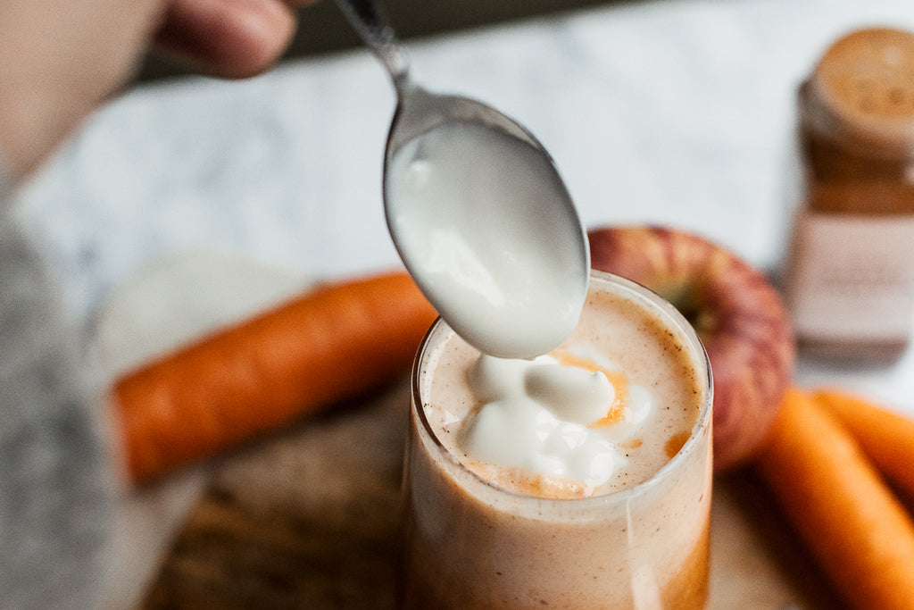 kefir yoghurt being added to glass of apple, ginger, carrot smoothie