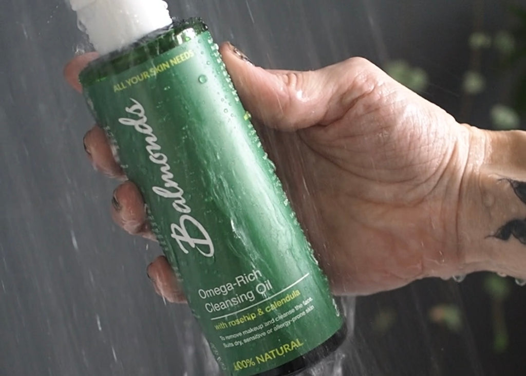 Close up hand in shower holding Balmonds Drench Ritual Body Oil