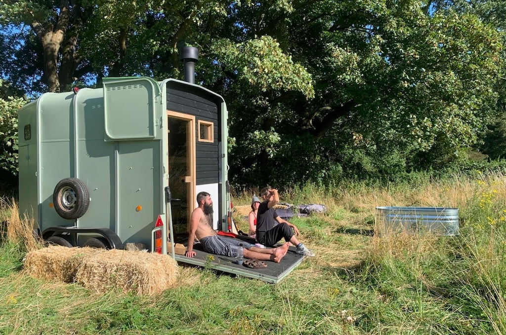 Group resting outside horsebox sauna in a field