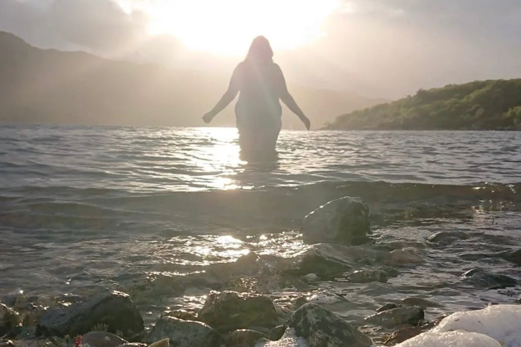 Wild Swimming - nic Goddard, Scotland. Silhouette against the sun stepping into cold water from the shore