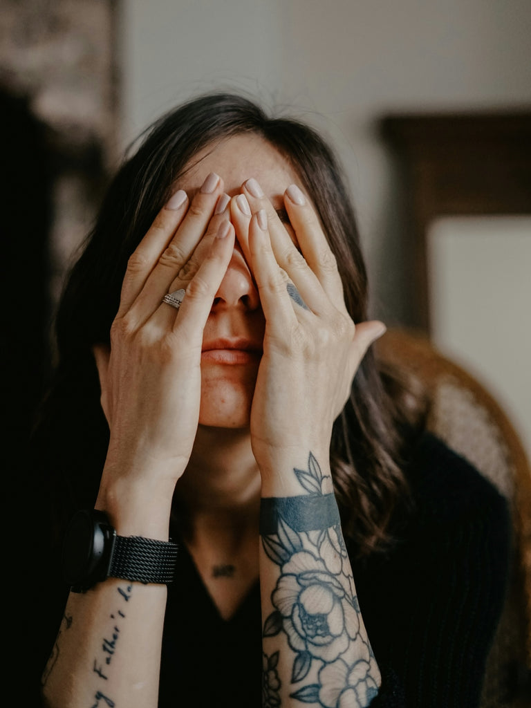 woman with tattoos with her head in her hands reflecting stress