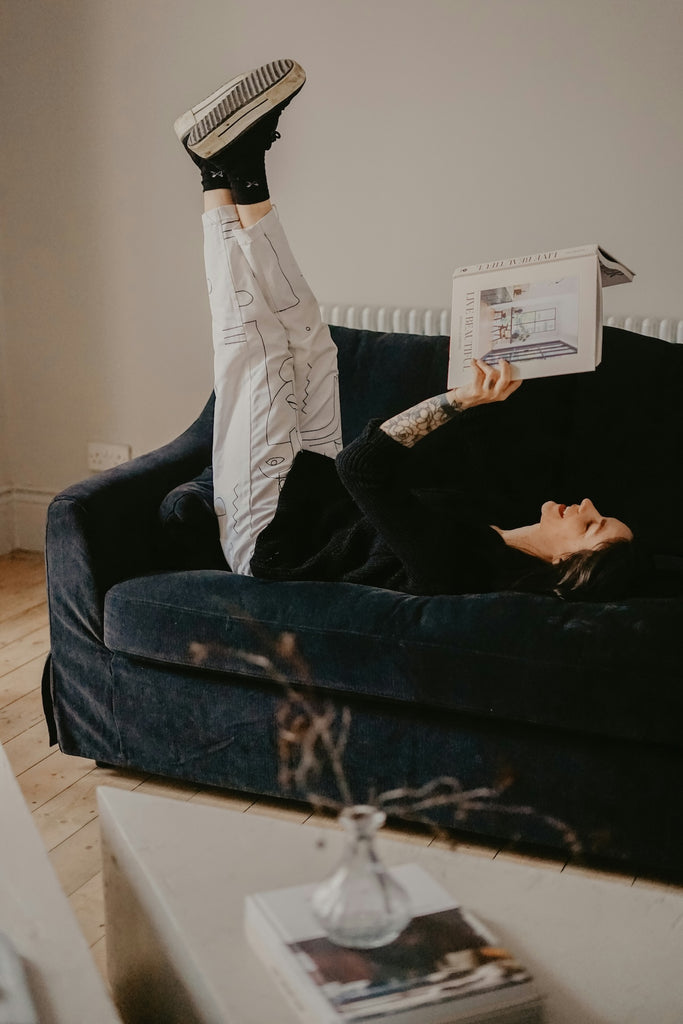woman reading a book for mental wellbeing and moments of joy. She is lying on a sofa with her legs kicked up reflecting positive emotions