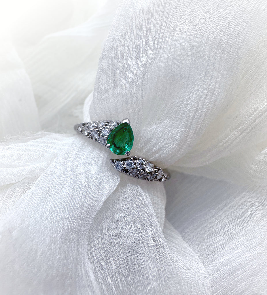 A large pear-cut emerald is set into an elegantly-shaped wrap ring studded with diamonds.