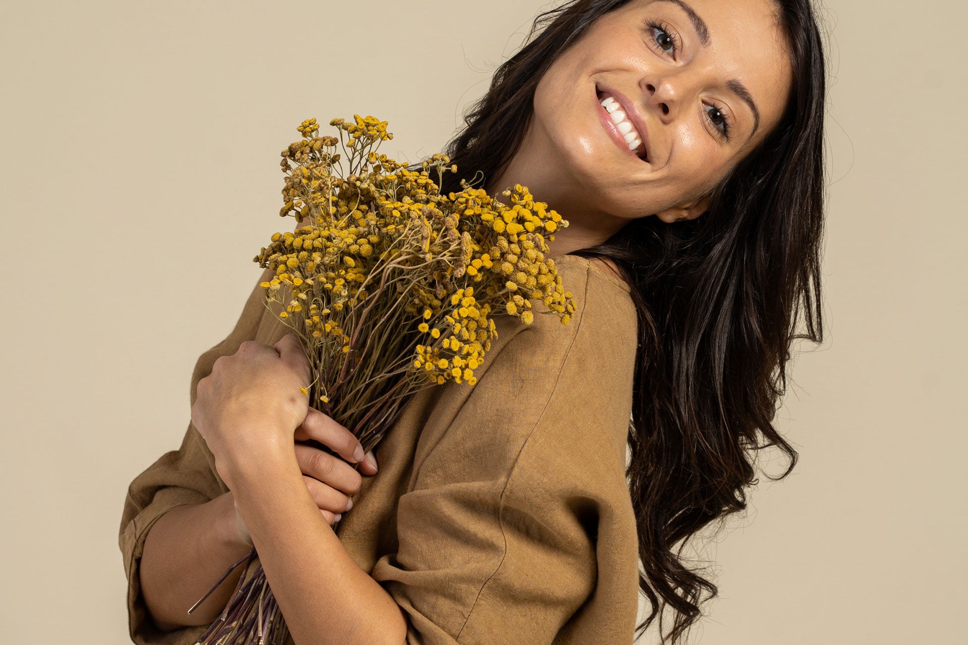 Woman wearing caramel brown linen tunic and holding flowers in her hands