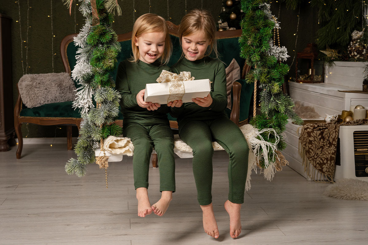 Zwei kleine Mädchen auf der Schaukel, die das Weihnachtsgeschenk betrachten