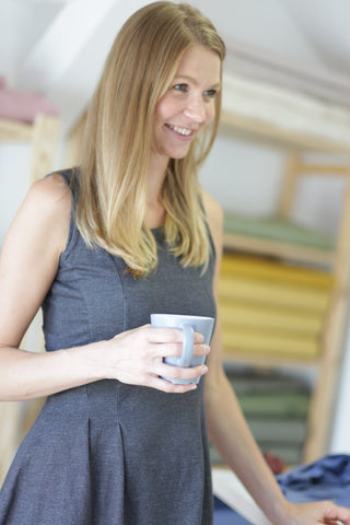 Liane Mörtl aus Radeberg in ihrem Atelier, eine glücklich aussehende Frau steht vor einem Stoffregal und hält eine Tasse in der Hand
