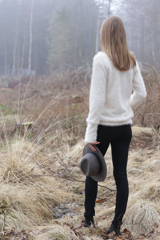 Eine Frau trägt eine schwarze Jeans und einen weißen Pullover und hält einen Hut in der Hand