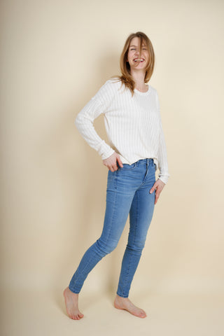 eine große blonde Frau trägt eine Jeans und ein handgemachtes Oberteil aus Leinenstrick