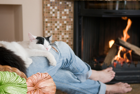 lady relaxing with her cat by a fireplace crocheting