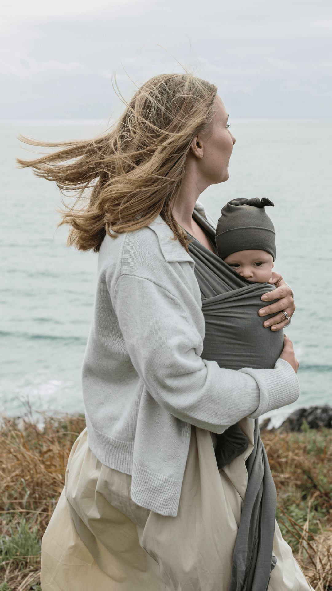 Mother holds baby in Sea Stone Solly Wrap with her hair blowing in the wind