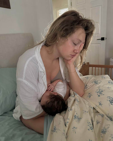 Tired woman sitting in bed breastfeeding baby