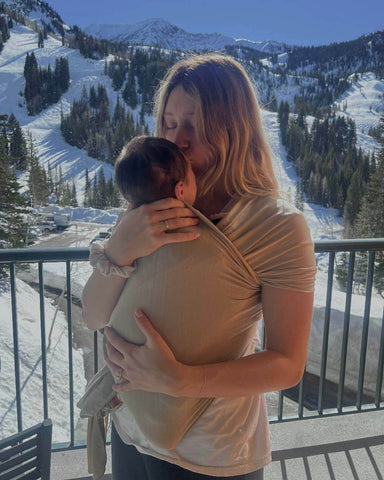 Woman kissing baby in Flax Solly Wrap with snowy mountains in the background