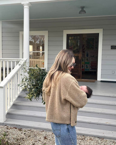 Woman holding baby walking to front porch of house.